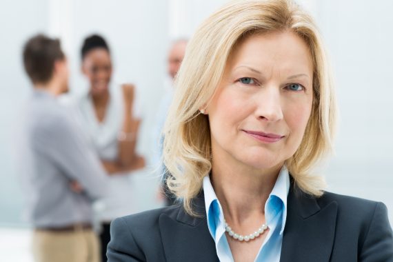 Team of office workers standing and talking with woman in front, facing camera