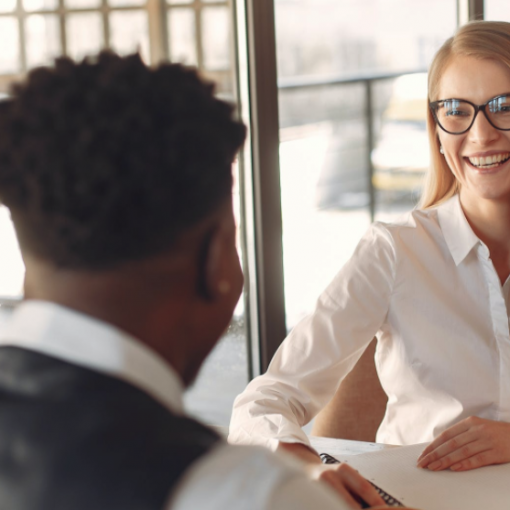 Coworkers sitting across from each other at a desk, smiling, writing tablets on desk. Photo by Gustavo Fring from Pexels.com.